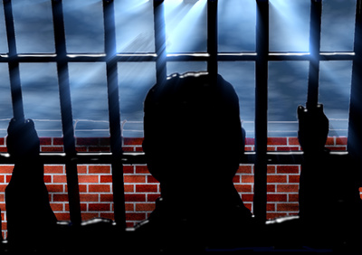 Mann hinter Gittern mit Blick nach außen auf eine Mauer